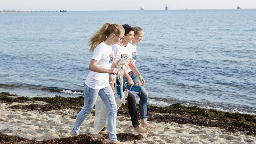 Foto, das drei Jugendliche am Ufer bei der Suche nach Plastik zeigt