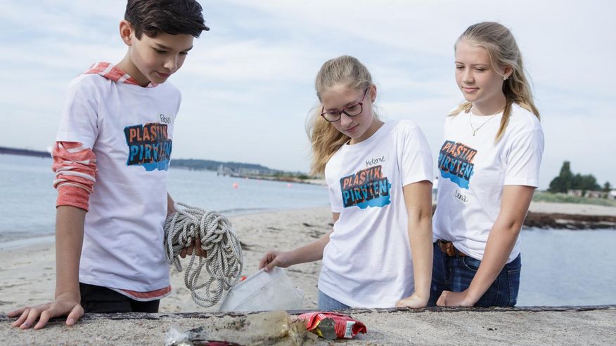 Foto, das zwei Schülerinnen und einen Schüler dabei zeigt, wie sie ihre Plastikfunde am Ufer auswerten