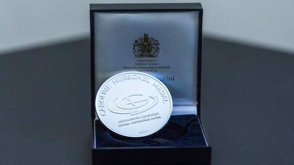 Eine silberne Medaille mit der Aufschrift „Caroline Herschel Medal, Astronomische Gesellschaft, German Astronomical Society“, die in einem geöffneten Kästchen liegt.
