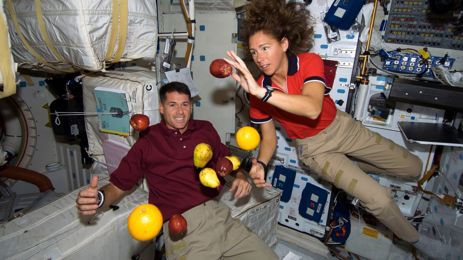 Ein Astronaut und eine Astronautin mit schwebendem Obst in einer Raumstation