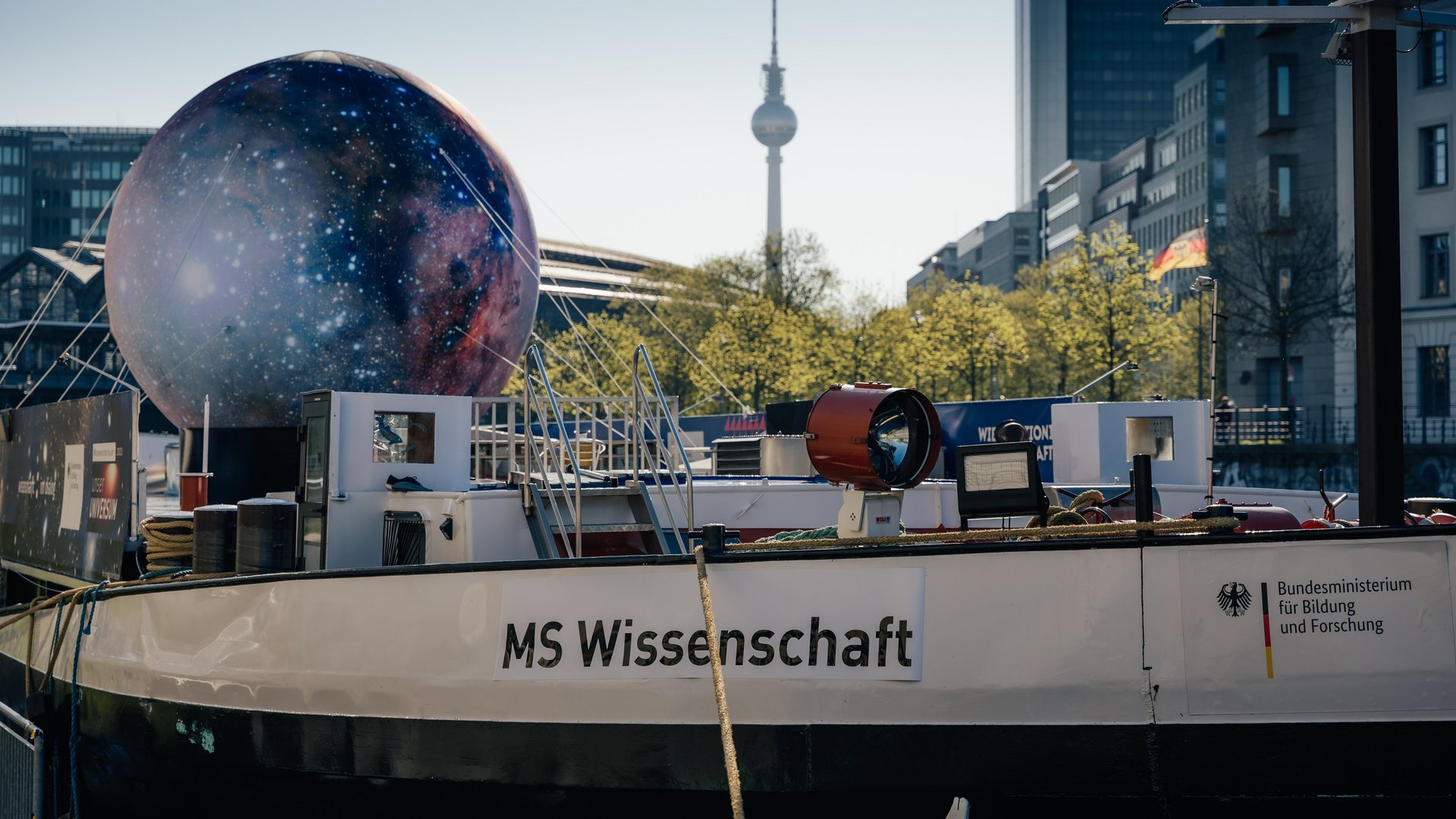Projektbild MS Wissenschaft: Foto eines Frachtschiffes, an der Reling steht "MS Wissenschaft" An Deck ist eine große Attrappe des Mondes mit Seilen befestigt.