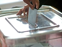 Zwei Hände werfen ihren Wahlschein in eine Urne