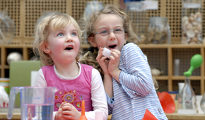 Zwei kleine Mädchen experimentieren mit Wasser und Trichtern und lachen.