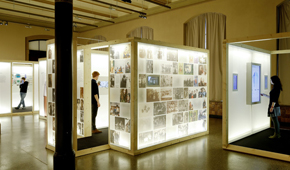 Ausstellungsraum mit beleuchteten Schauwänden und drei Besuchern