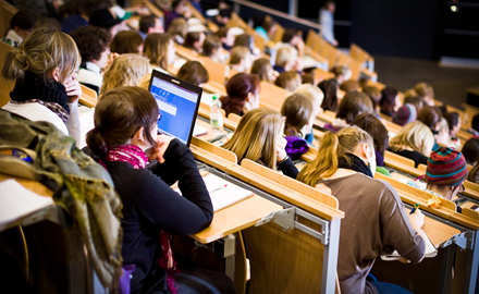 In einem modernen Hörsaal sitzen Studenten und schauen konzentriert in Richtung Tafel.