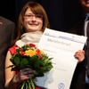 Anett Oefler im roten Kleid und mit Blumenstrauß bei der Meister-Verleihung.