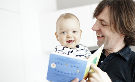 Ein Vater hält sein Baby auf dem Arm und zeigt ihm ein Bilderbuch.