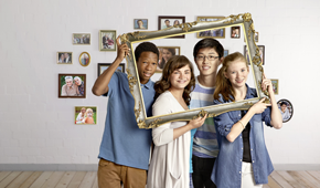 Vier Kinder vor einer Wand mit Bilderrahmen.