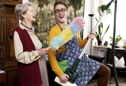 Ältere Frau und junger Mann putzen lachend die Wohnung