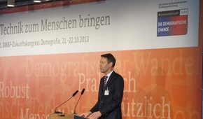 Staatssekretär Georg Schütte spricht vor einer orangefarbenen Rückwand beim Zukunftskongress in der Kalkscheune
