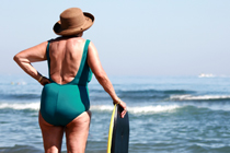 Ältere Frau mit Surfbrett schaut auf das Meer hinaus