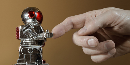 Das Bild zeigt einen kleinen Roboter, der einem menschlichen Zeigefinder die Hand gibt