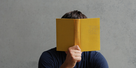 Das Bild zeigt eine Person, die sich ein Buch vor das Gesicht hält