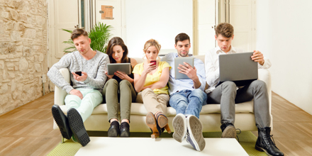 Freunde sitzen auf dem Sofa mit ihren Smartphones und Tablets.