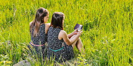 Zwei Mädchen sitzen auf Stein mit Smartphones in den Händen.