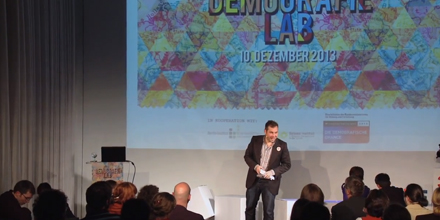 Link zum Youtube-Video/ Bild zeigt den Moderator der Veranstaltung auf der Bühne