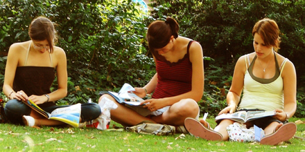 Drei Frauen sitzen auf einer Wiese und lesen.