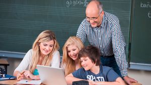 Lehrer und Schüler schauen auf PC