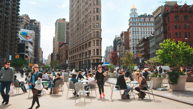 Szene aus The Human Scale: Menschen sitzen an Café-Tischen auf einem großen Platz einer Stadt