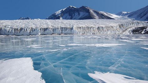 Bruechige Eisplatten auf blauem Wasser vor dem Panorama eines Gletschers