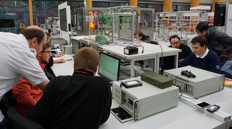 Studierende sitzen um einen Arbeitsplatz mit Computern und untersuchen digitale Lösungen für smarte Fabriken oder Städte