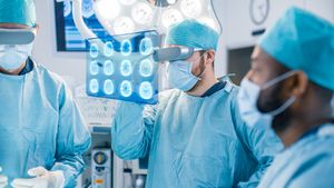 Surgeons Wearing Augmented Reality Glasses Perform State of the Art Augmented Reality Surgery in High Tech Hospital. Surgeon Looks at Brain Scans and Medical History of the Patient.