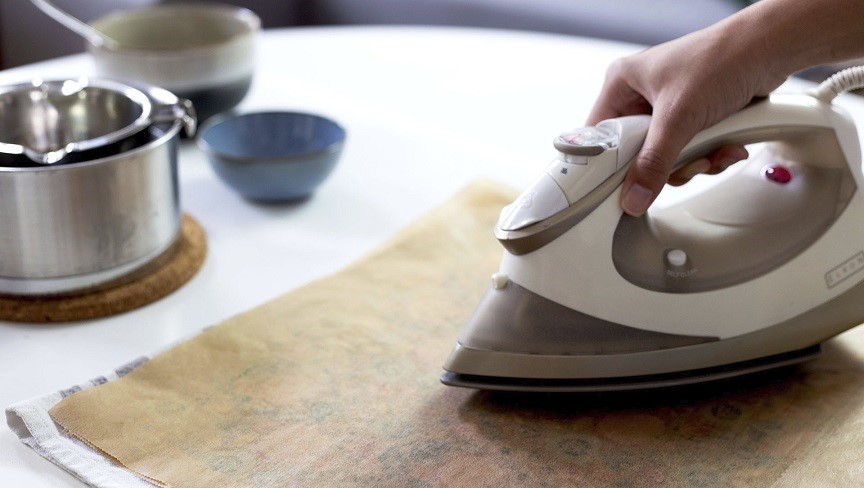 Eine weibliche Hand fährt mit einem Bügeleisen über Backpapier, das sich über den bestrichenen Tüchern befindet