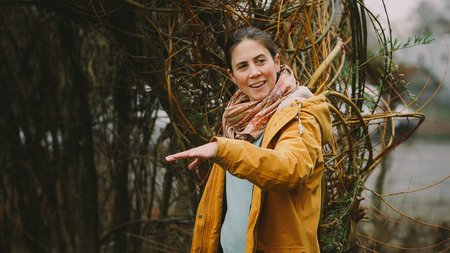 Frau steht erklärend vor einem Baum
