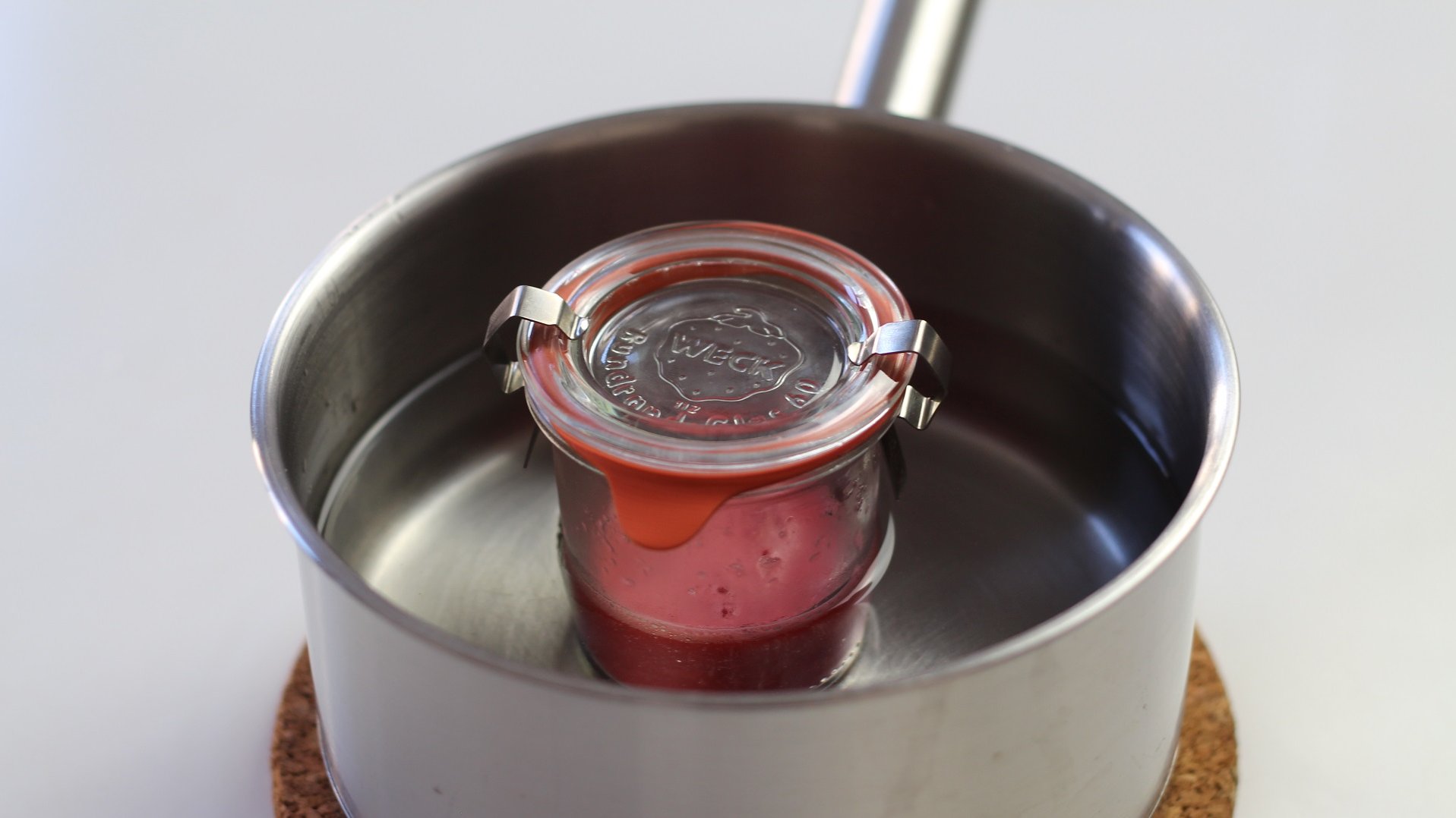 Ein Glas mit einem roten Inhalt in einem mit Wasser gefüllten Kochtopf.