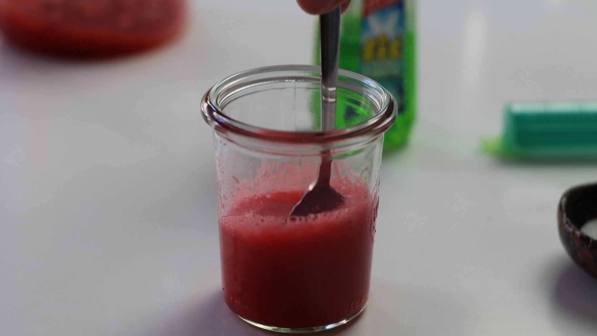 Rote Lösung in einem Glas wird mit einem Teelöffel verrührt.