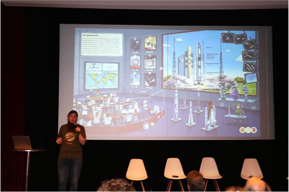 Michael Büker steht vor einer Leinwand und spricht in ein Mikrofon.