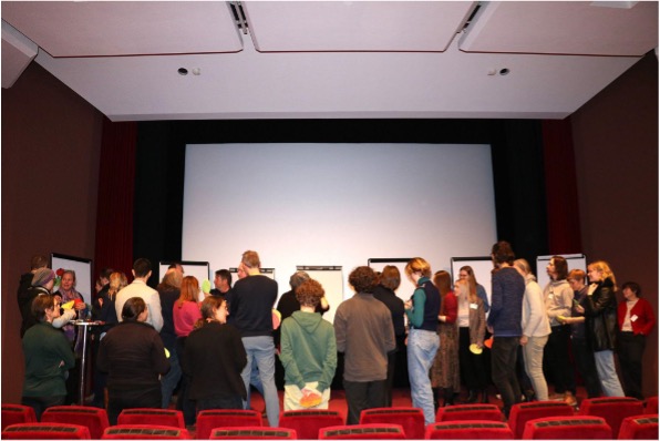 Eine Gruppe Menschen von hinten. Sie stehen vor einer Leinwand. 