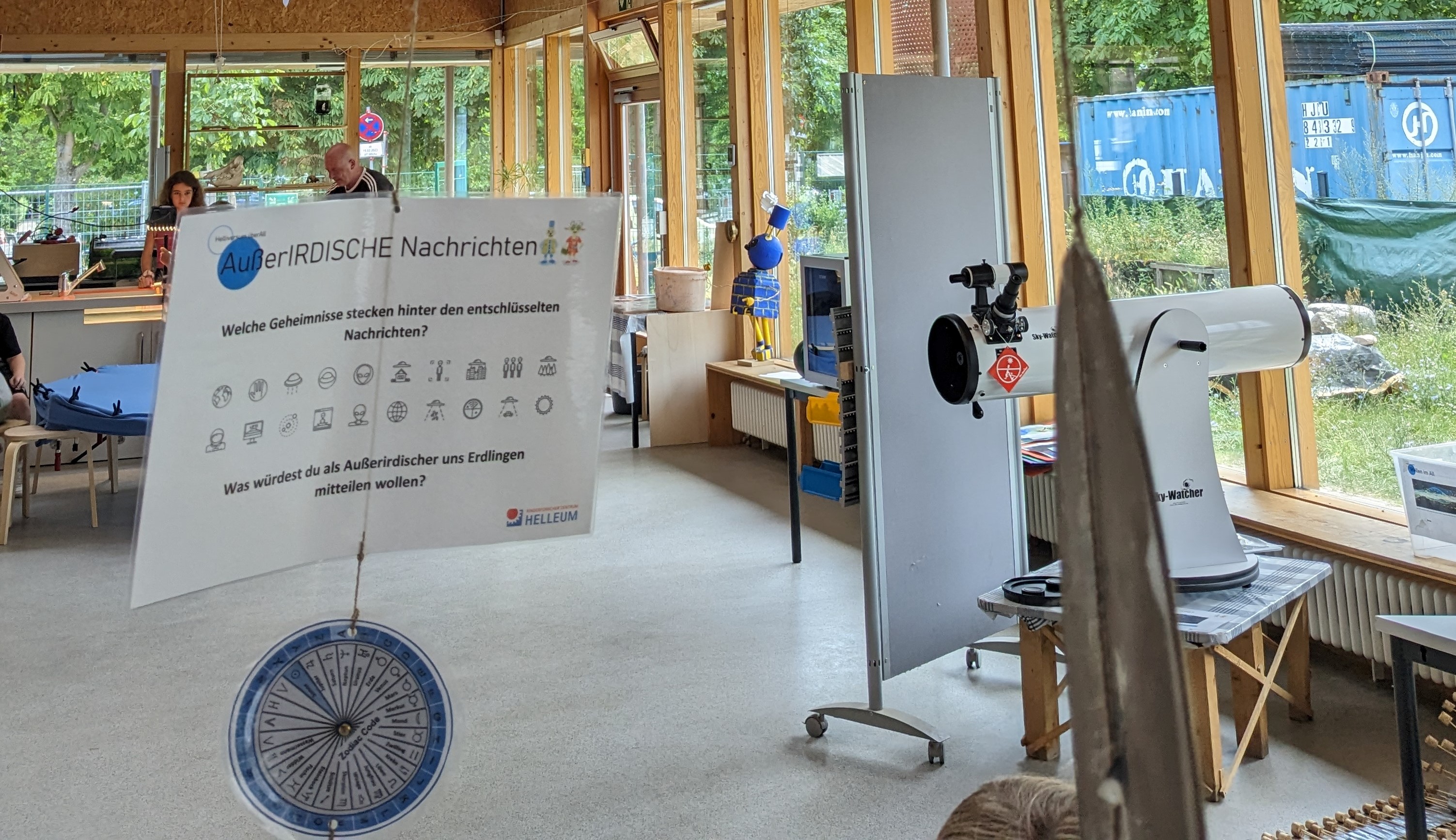 Lichtdurchfluteter Raum mit Stelltafeln und Teleskop 