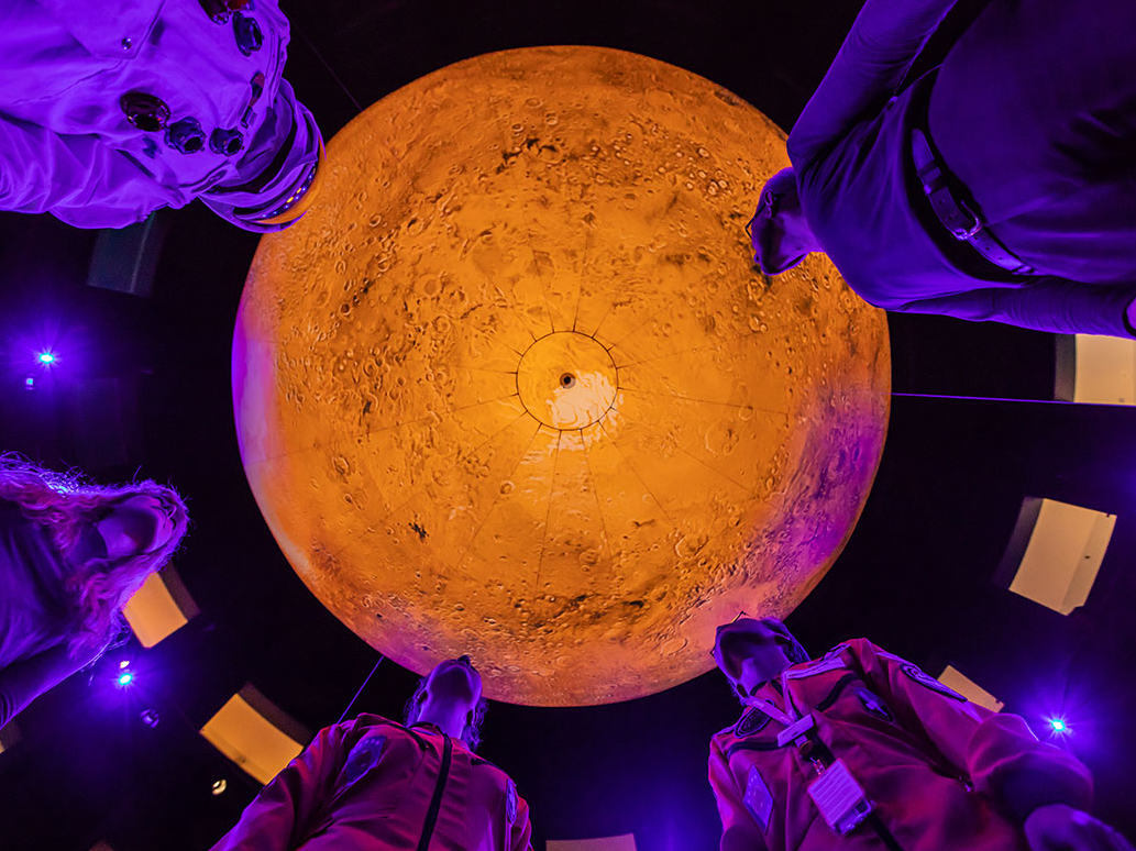 Einige Leute stehen im Kreis um das orange leuchtende Marsmodell