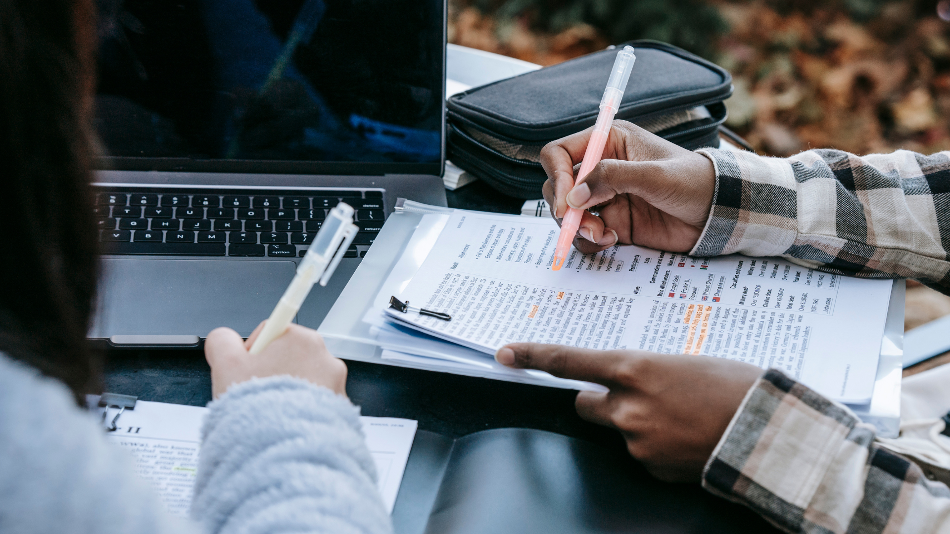 Foto von zwei Schüler*innen, die für die Schule arbeiten. Einer markiert einen Text, die andere schreibt auf einem Block.