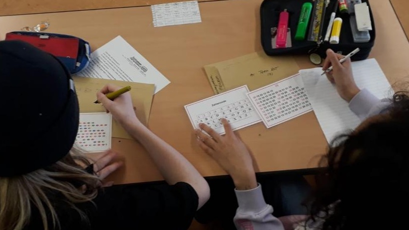 Zwei Schüler*innen sitzen an einem Schultisch und bearbeiten Arbeitsblätter. 
