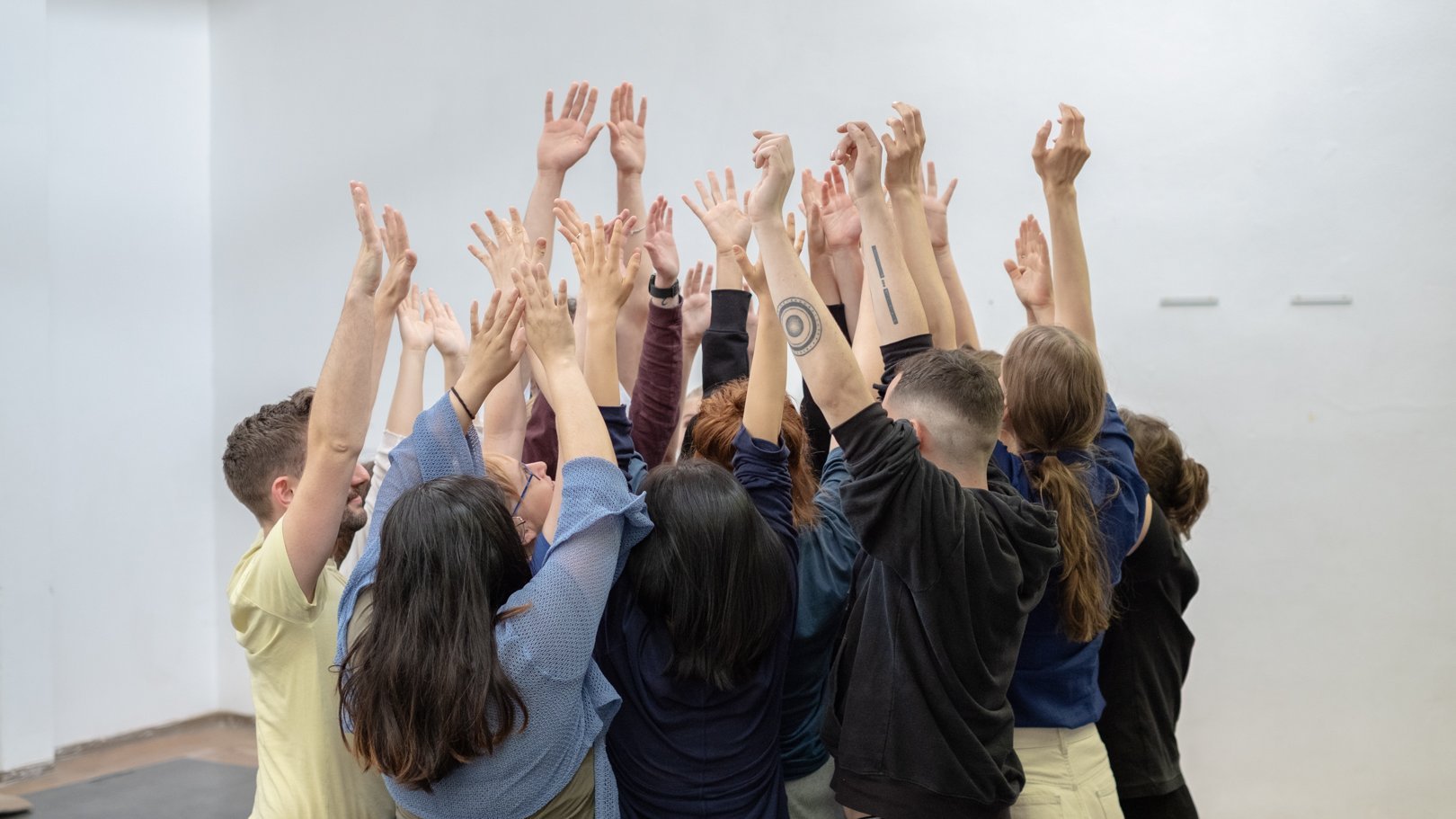 Gruppe junger Menschen steht zusammen, alle heben die Hände 