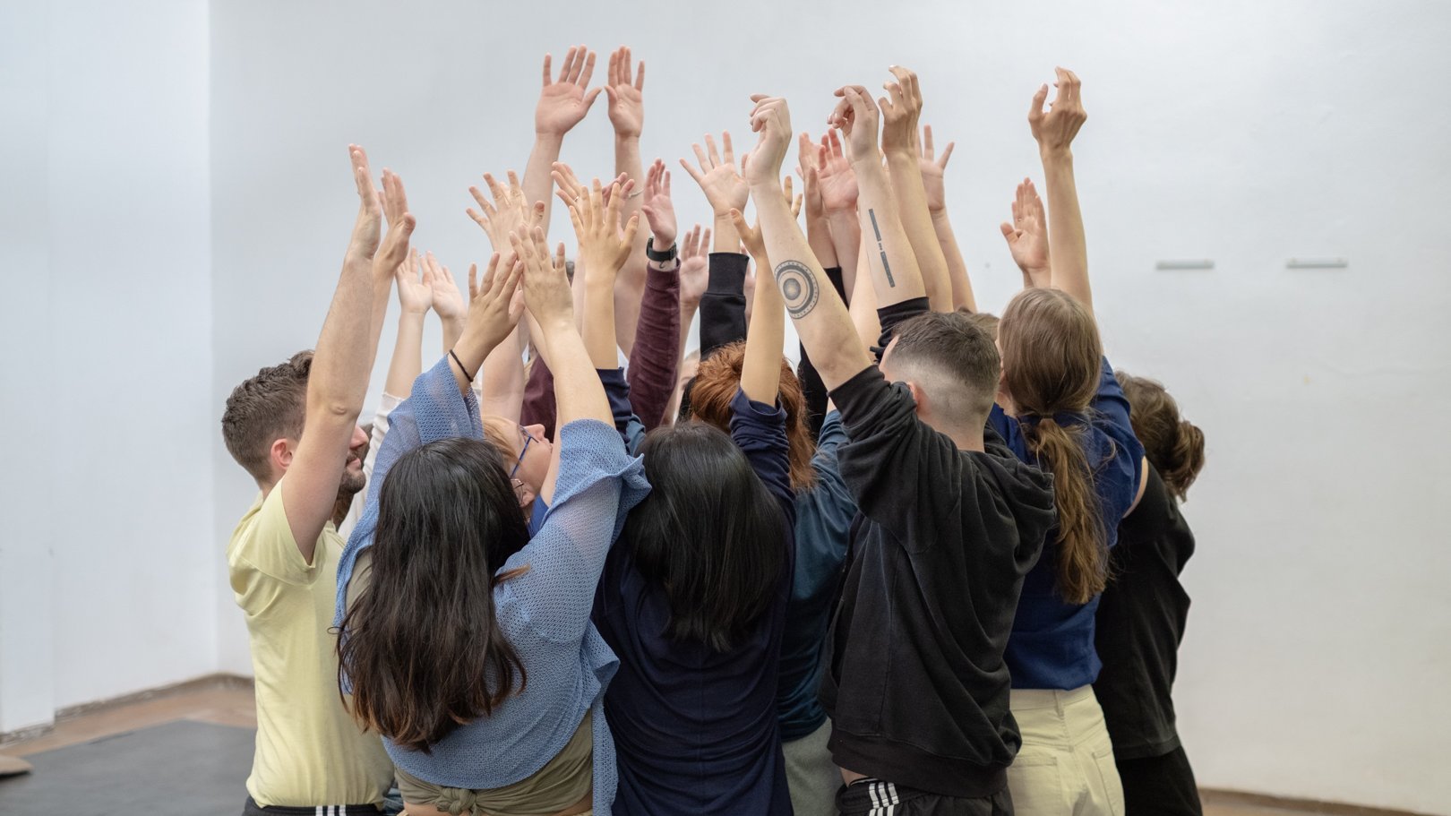 Gruppe junger Menschen steht zusammen, alle heben die Hände 