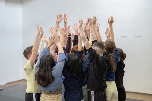 Gruppe junger Menschen steht zusammen, alle heben die Hände 