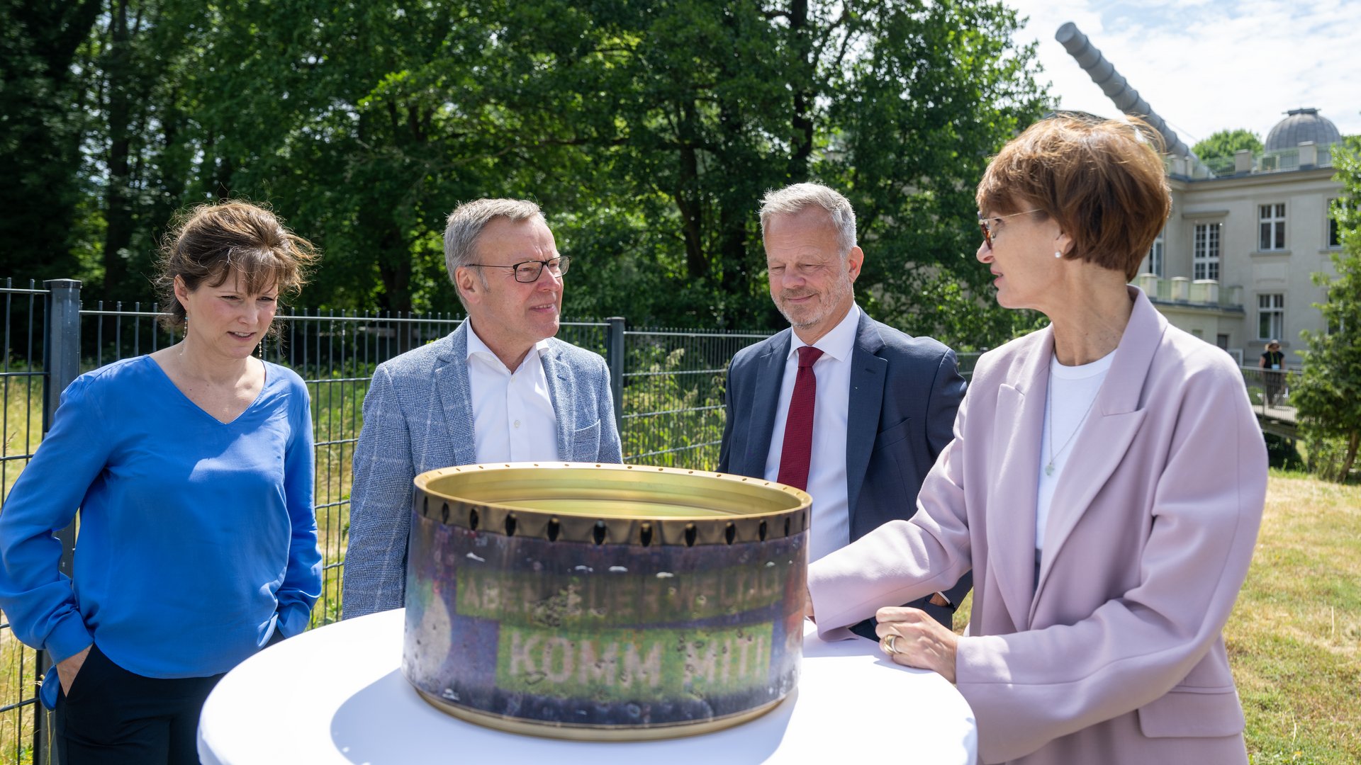 Vier Personen stehend an einem Tisch, draußen