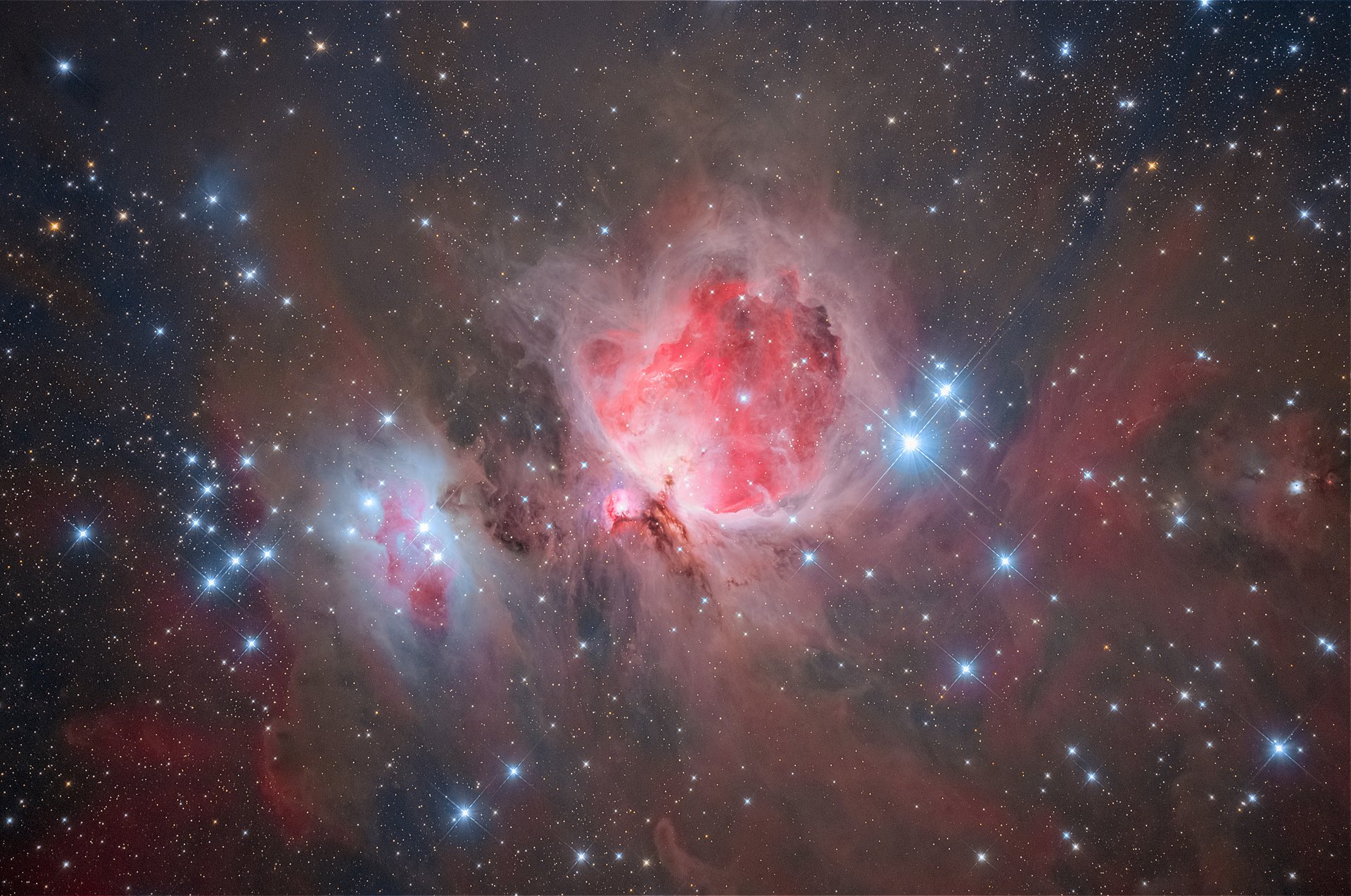 In der Mitte ist eine rosa leuchtende Galaxie zu sehen. Blau leuchtende Sterne umgeben sie.