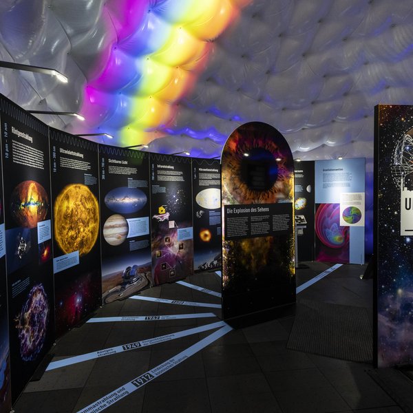 Foto der Ausstellung im Zelt, im Hintergrund ist ein kleiner Regenbogen