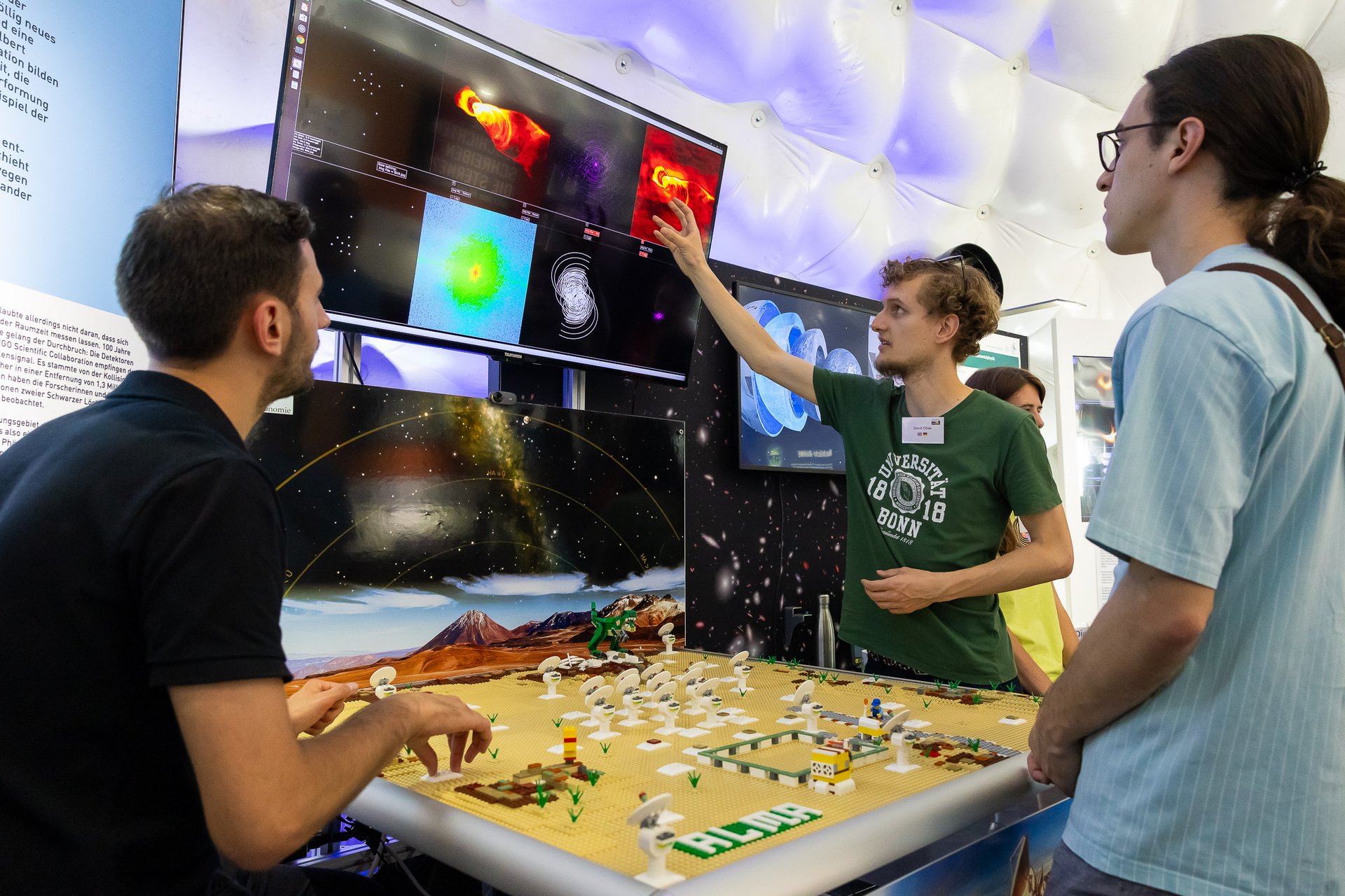 Ein Mann zeigt auf einen Bildschirm in der Zeltkuppel und erklärt zwei weiteren Leuten etwas