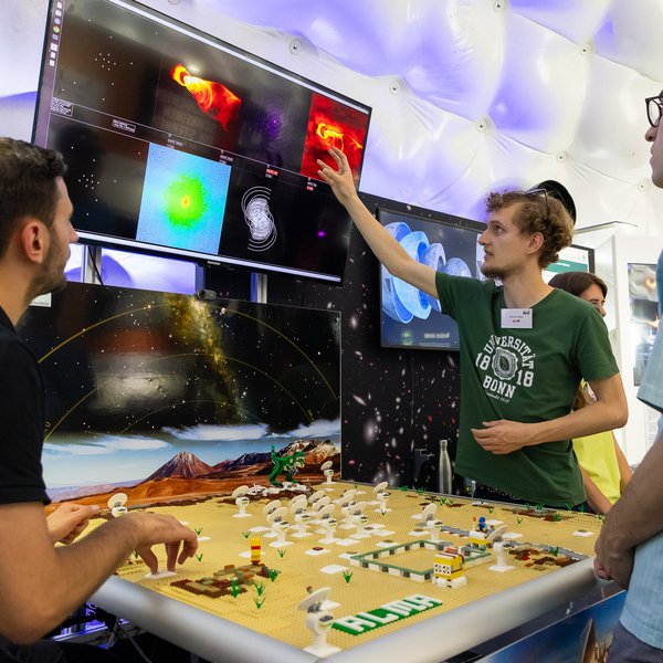 Ein Mann zeigt auf einen Bildschirm in der Zeltkuppel und erklärt zwei weiteren Leuten etwas