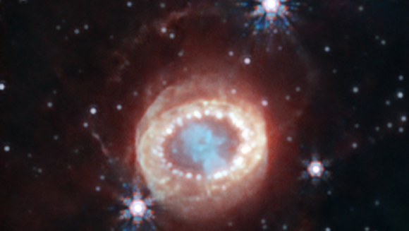 Auf schwarzem Hintergrund leuchtet ein oranger Kreis, darin eine verschwommene blaue Struktur umgeben von einem Oval aus weißen Punkten. 