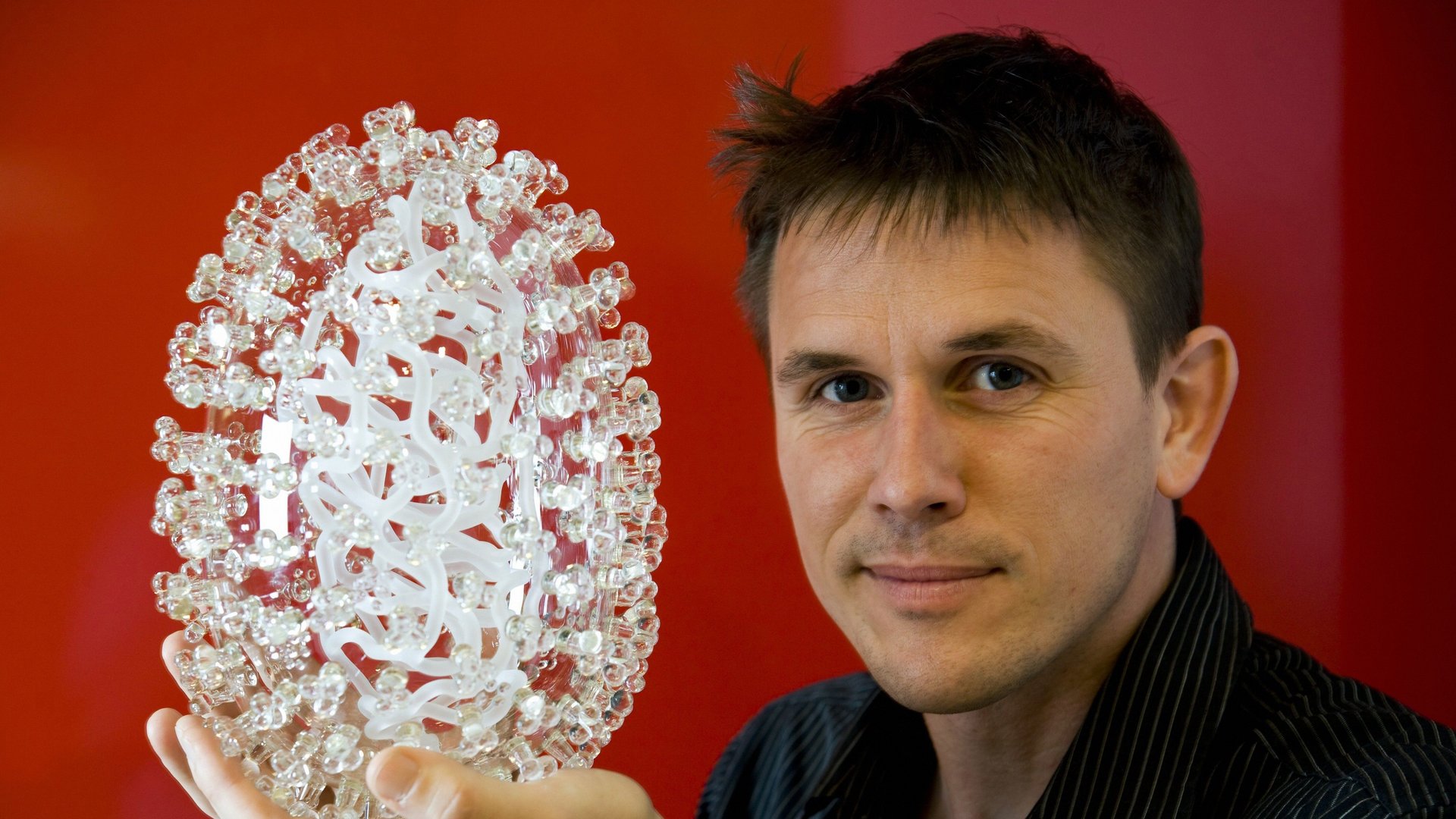Ein Porträt von dem Künstler Luke Jerram. Er hält ein weißes Modell in der Hand.