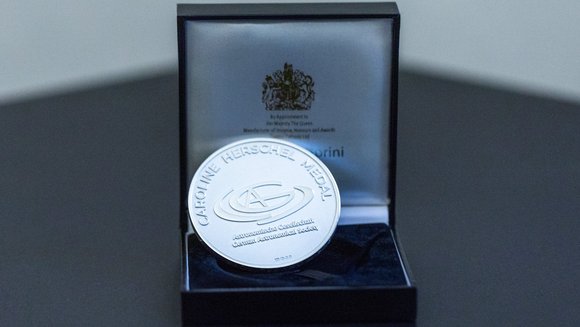 Eine silberne Medaille mit der Aufschrift „Caroline Herschel Medal, Astronomische Gesellschaft, German Astronomical Society“, die in einem geöffneten Kästchen liegt.