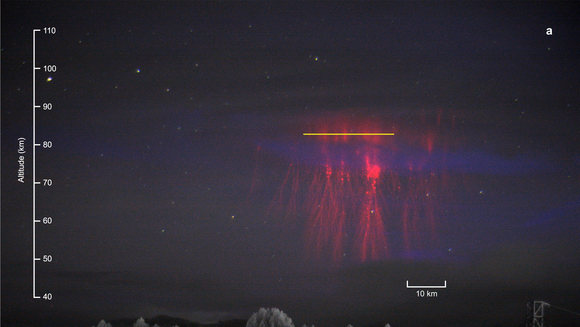 Baumkronen am unteren Rand, darüber ein rotes Leuchten. Im oberen Bereich des Leuchtens ist eine gelbe horizontale Linie, die den Spalt des Spektrografen, mit dem das Team die Messungen gemacht hat, auf das Bild projiziert.  