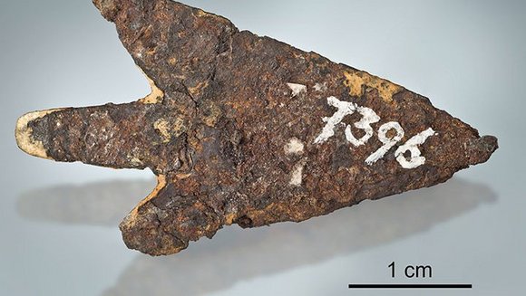 Ein Stück rostiges Eisen in Pfeilform, darauf ist in weiß die Zahl 7396 geschrieben. 