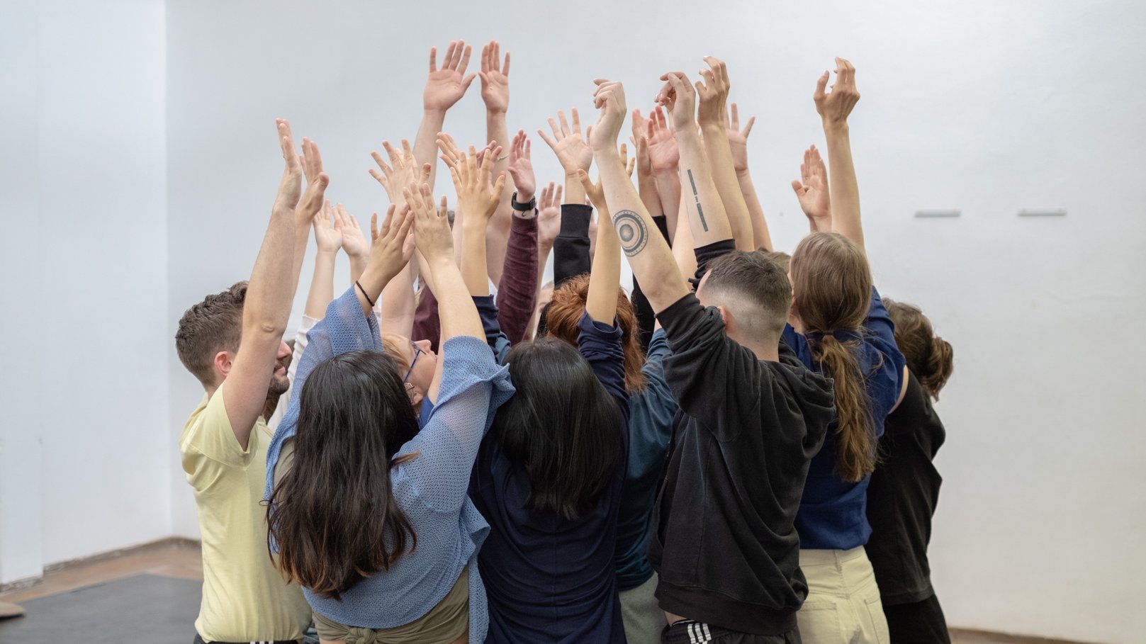 Gruppe junger Menschen steht zusammen, alle heben die Hände 